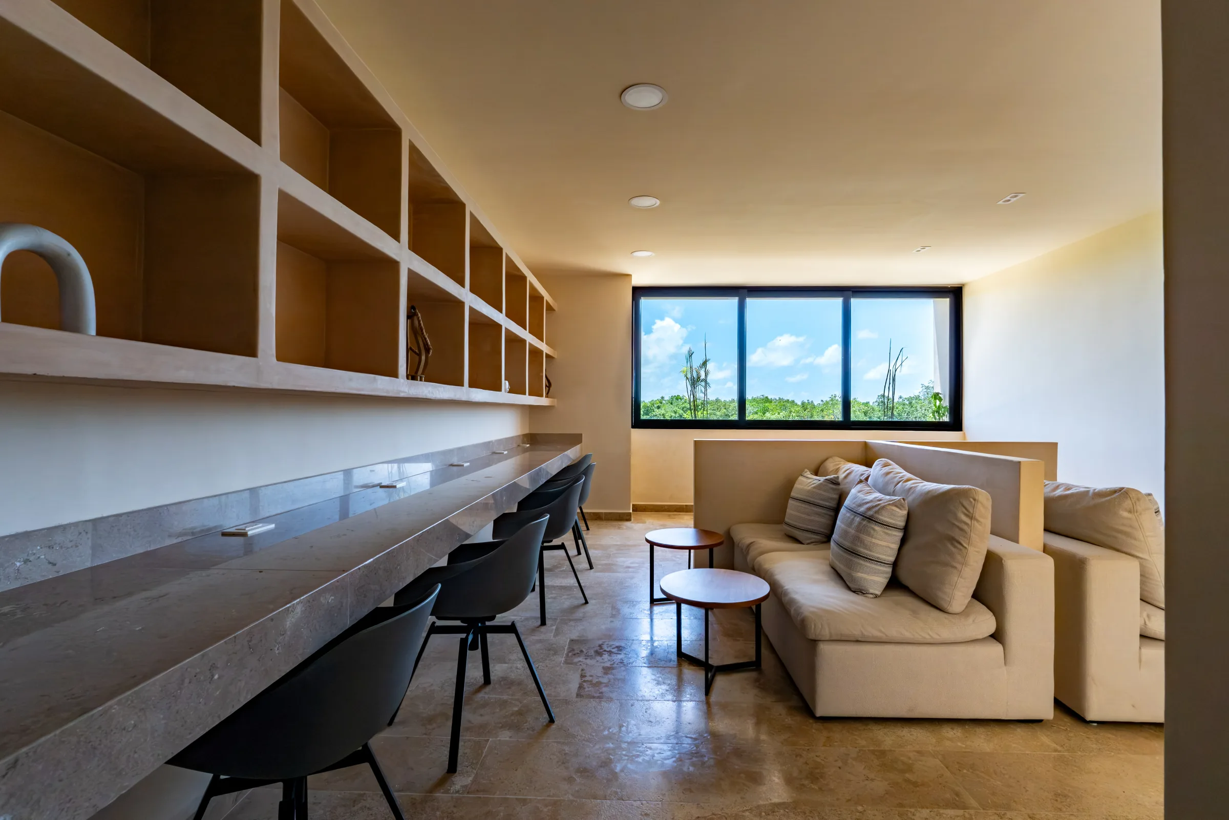Coworking con barra de trabajo, sillas y sala junto a un ventanal